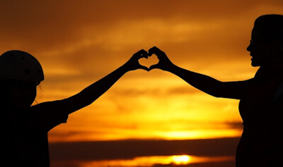 Due mani che si incontrano nel simbolo del cuore, su uno sfondo di tramonto dorato